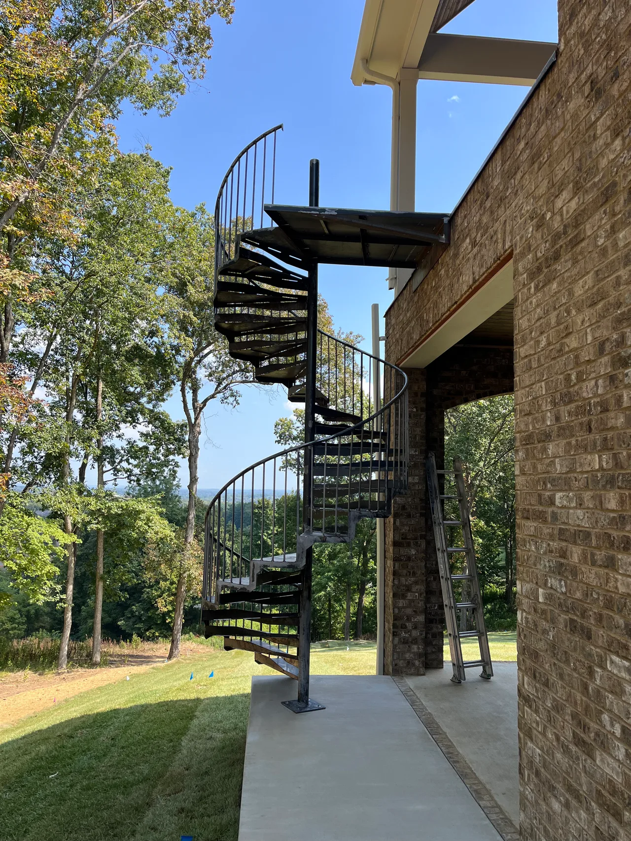 Custom metal spiral staircase with curved handrails beside a brick home